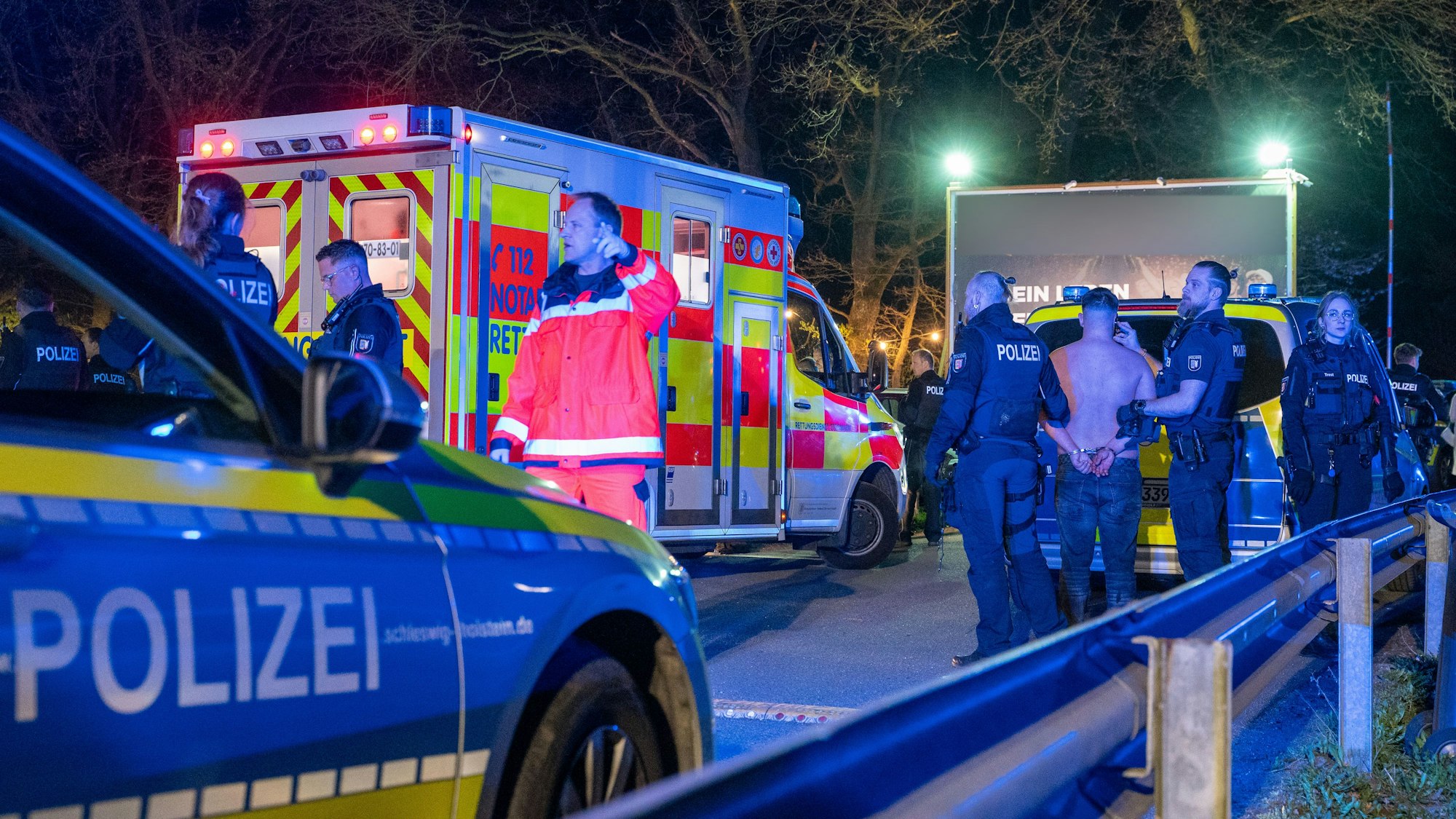 Polizisten und Rettungskräfte stehen an einer Disco mit einer Person, die festgenommen wurde.