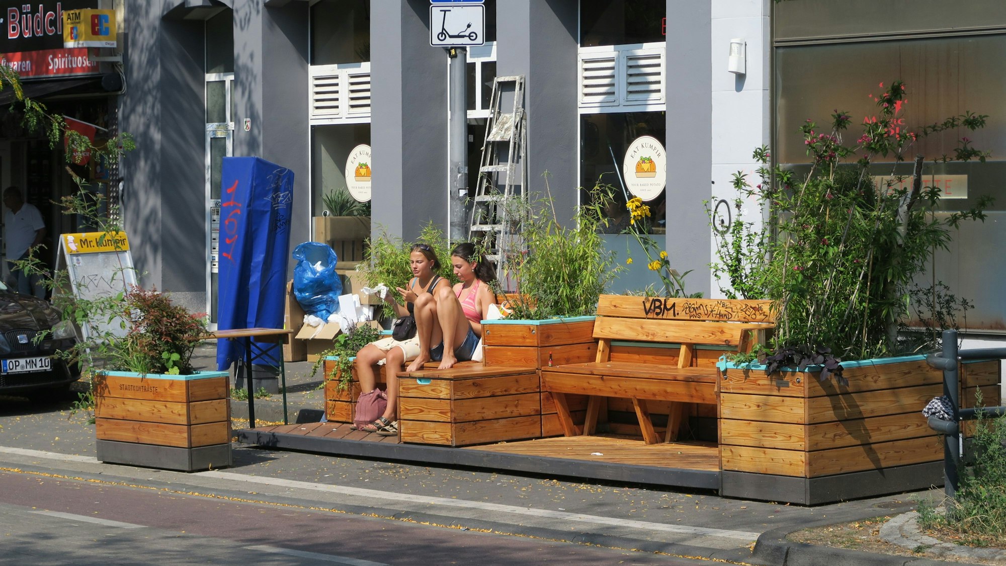 Zwei Mädchen sitzen auf Holzmöbeln an der Venloer Straße.