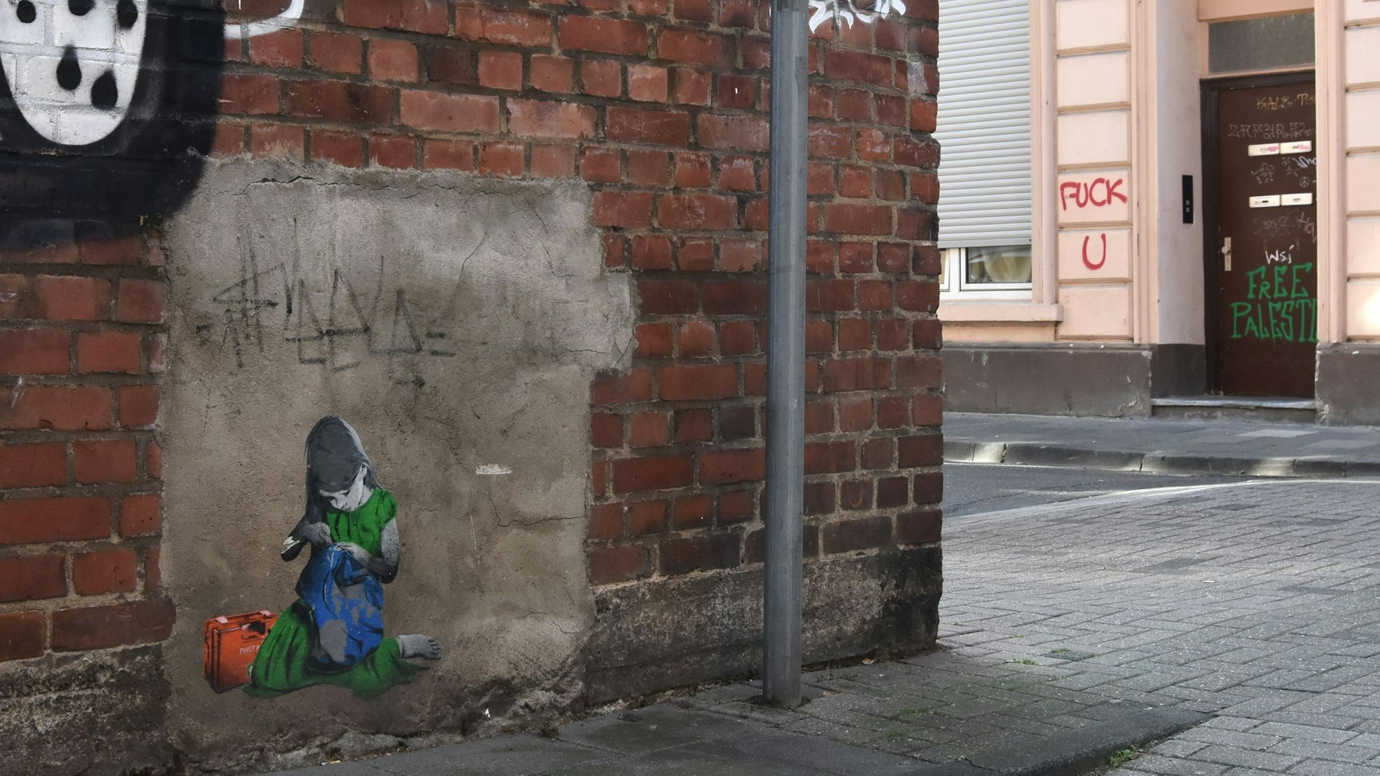 Ein Straßen-Graffiti zeigt ein Mädchen in einem grünen Kleid, das versucht, die Erde mit einem Erste-Hilfe-Set zu flicken