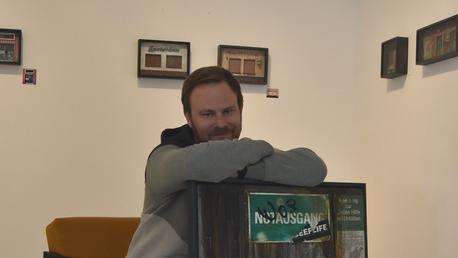 Ein Mann sitzt auf einem senfgelben Sessel und lehnt sich auf ein Graffiti-Werk.