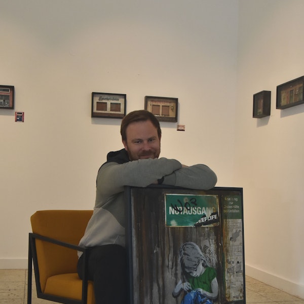 Ein Mann sitzt auf einem senfgelben Sessel und lehnt sich auf ein Graffiti-Werk.