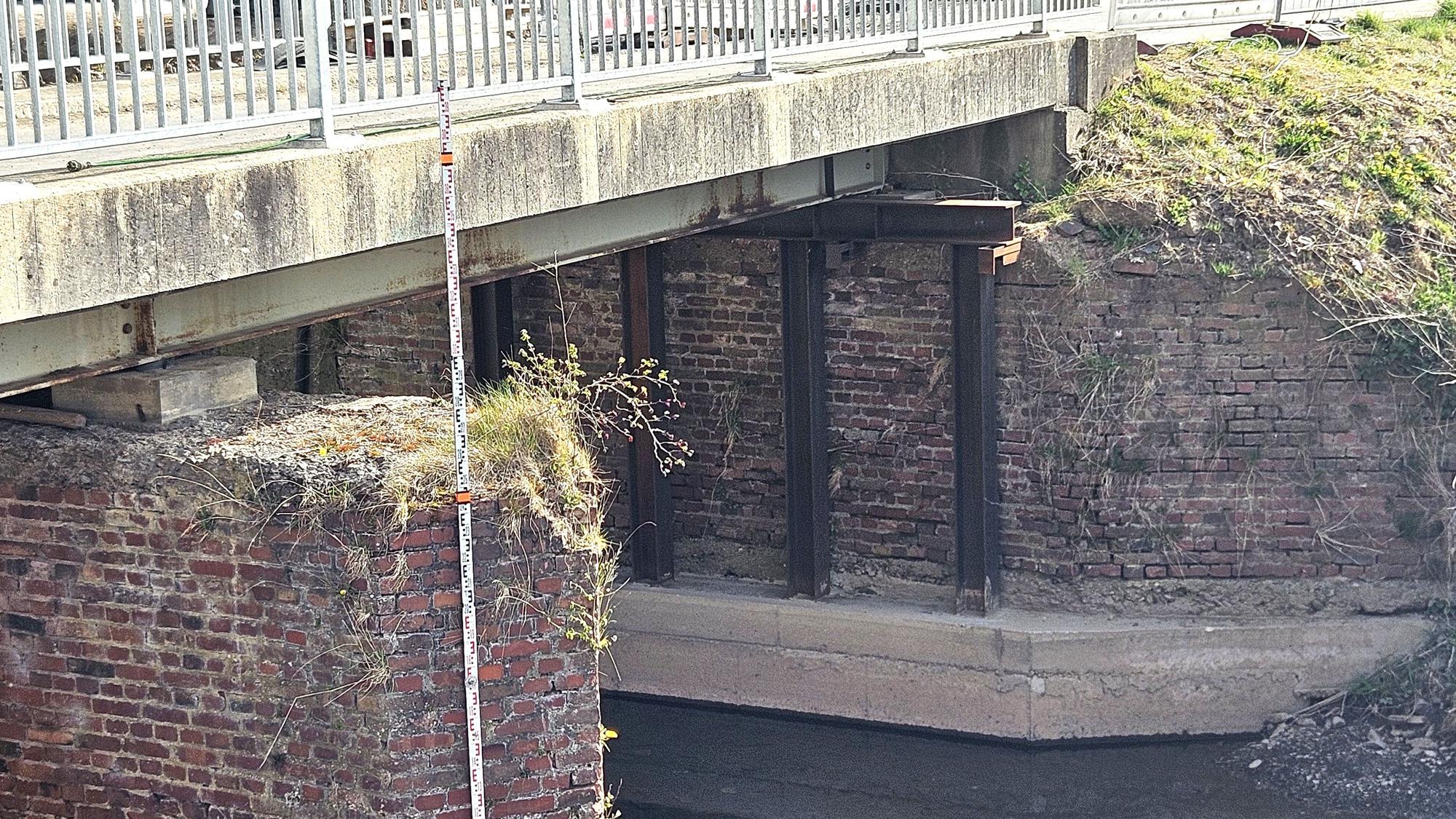 Blick auf den Bereich unter der Brücke mit Betonfundament und Eisenträgern.
