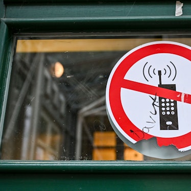 Ein Schild mit einem durchgestrichenen Handy-Symbol weist in einer Schule auf das Handyverbot hin. B