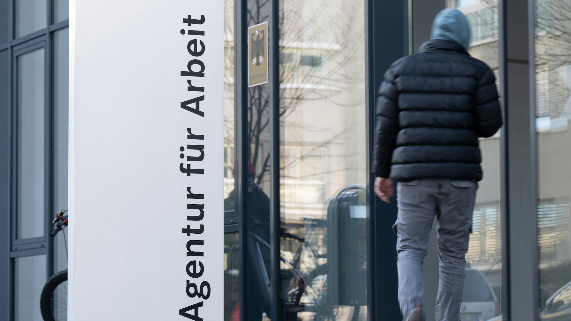 Ein Mann geht hinter einer Stele mit der Aufschrift „Agentur für Arbeit“.