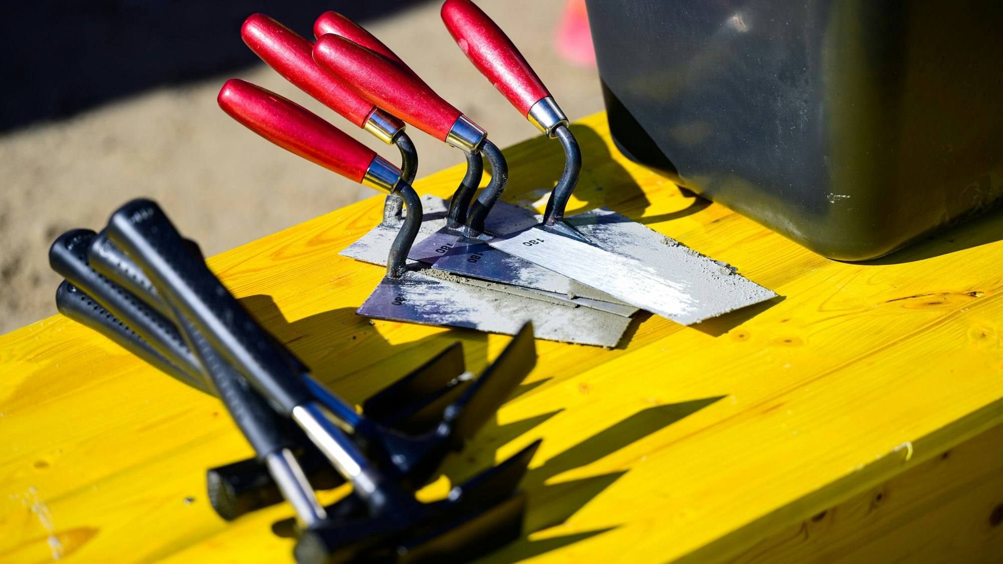 Maurerhammer und Maurerkellen liegen auf einer Baustelle.