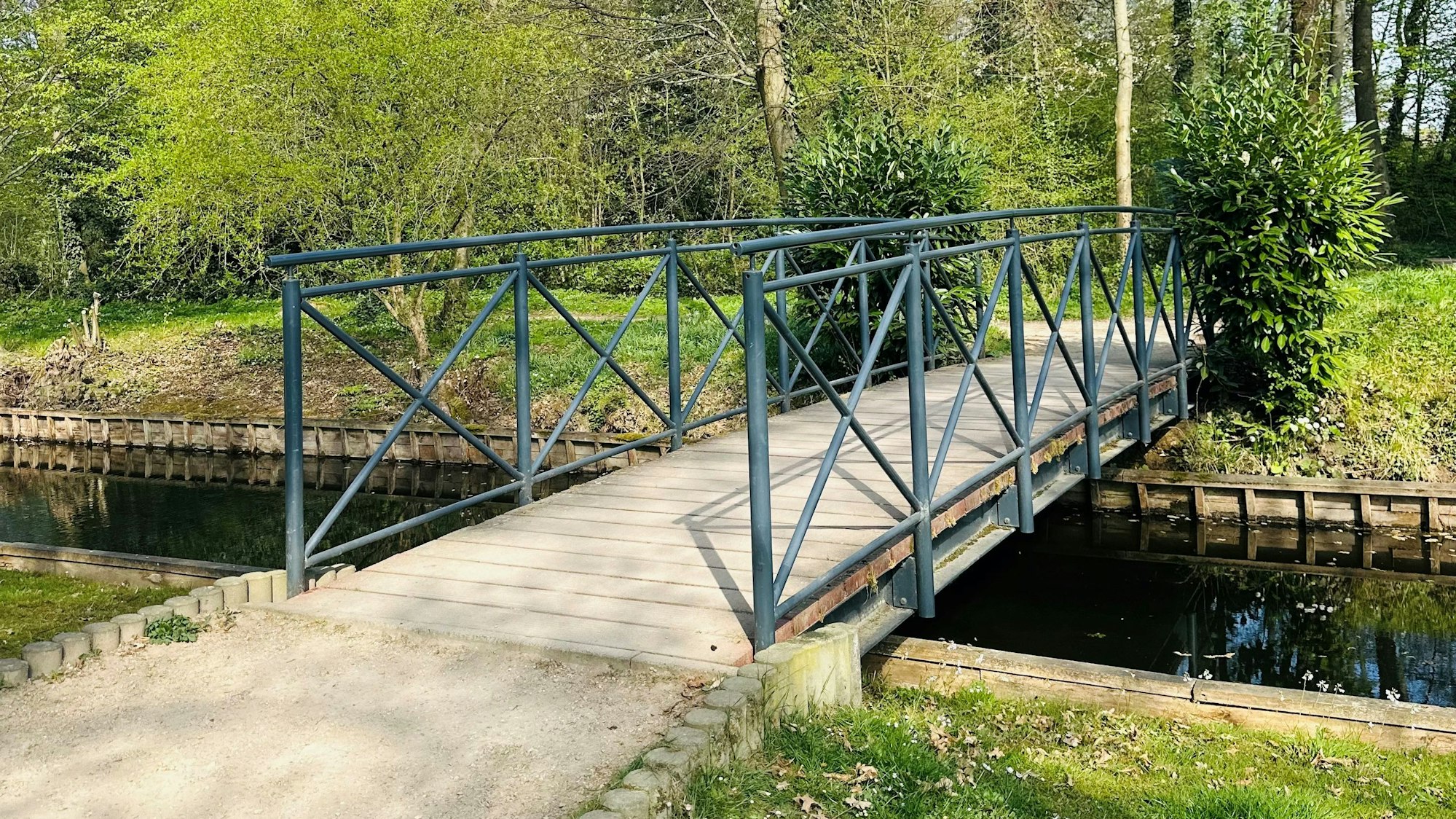 Zu sehen ist eine Brücke im grünen Schlosspark Gracht.