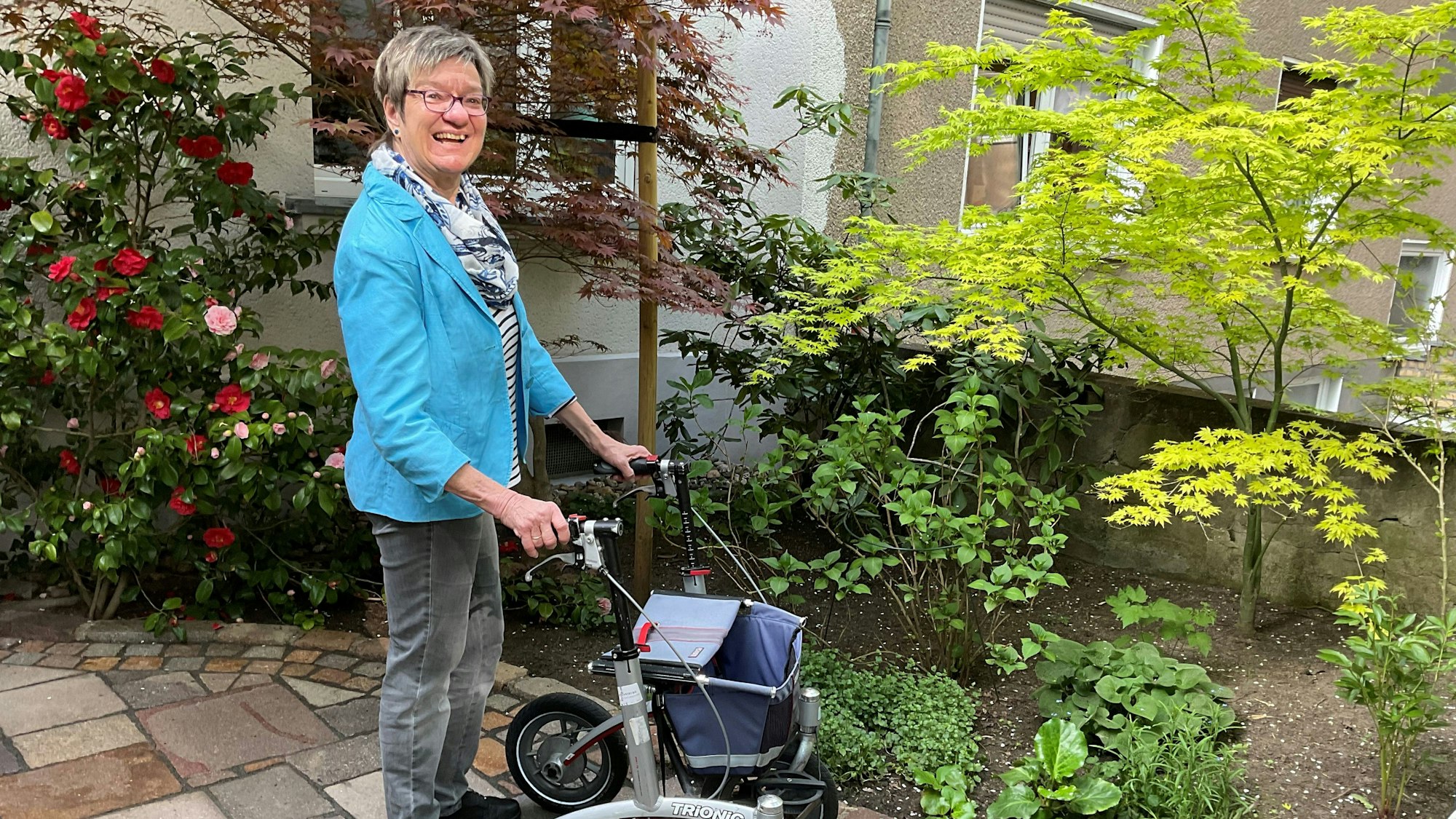 Eine Frau mit Kurzhaarschnitt und Brille sitzt an einem Tisch, vor sich ein Glas Latte Macchiato und ein Buch.