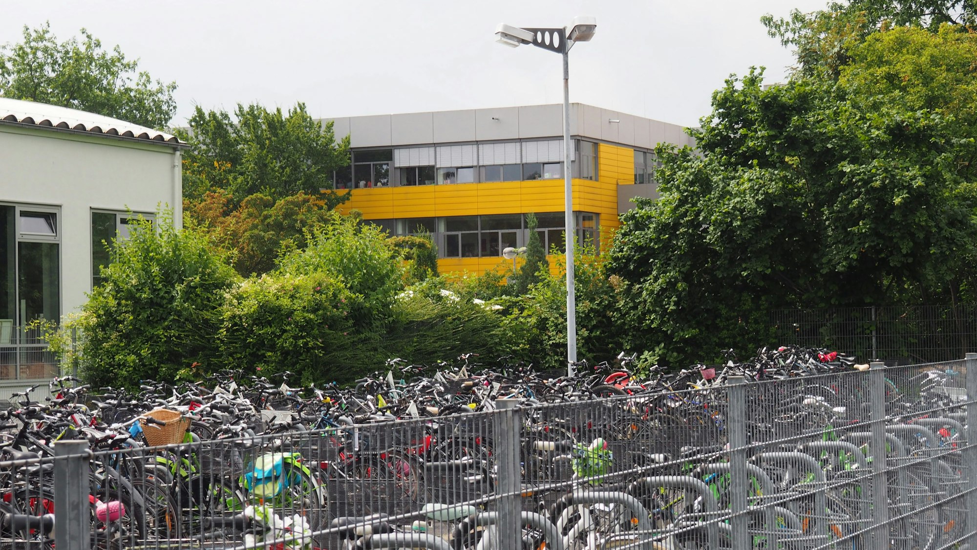 Im Vordergrund stehen viele Fahrräder, im Hintergrund ist ein Gebäude mit einer in Teilen sonnengelben Fassade zu sehen.