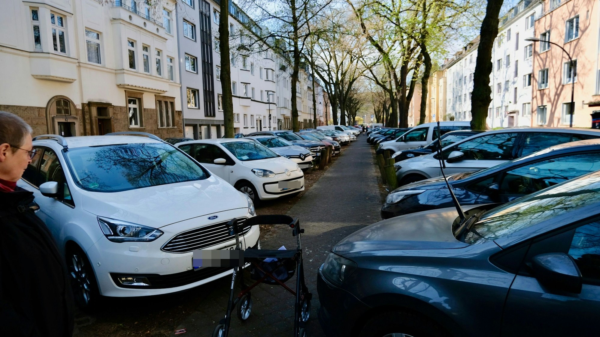 Blick auf den Mittelstreifen einer Straße, der von quer parkenden Autos zugestellt ist.