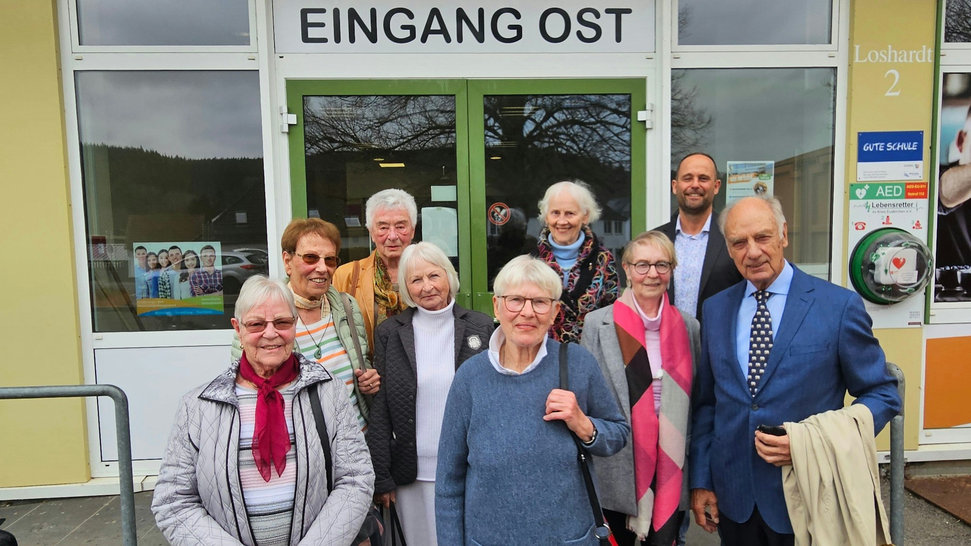 Die Frauen und ein Mann aus dem ersten Jahrgang stehen mit Schulleiter Holger Mohr vor dem Eingang zum Berufskolleg.