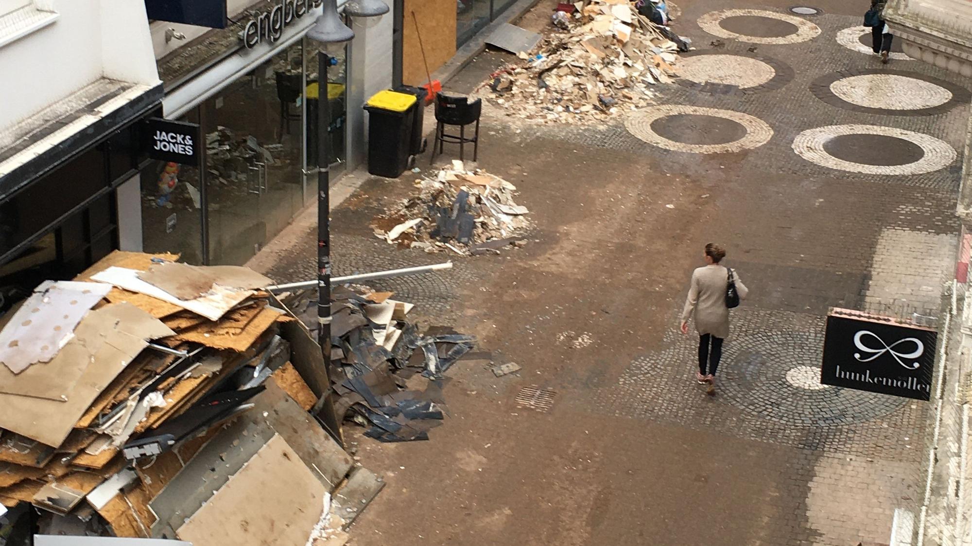 Das Bild zeigt die Neustraße, eine Passantin schaut auf Berge von Sperrmüll und Schutt.