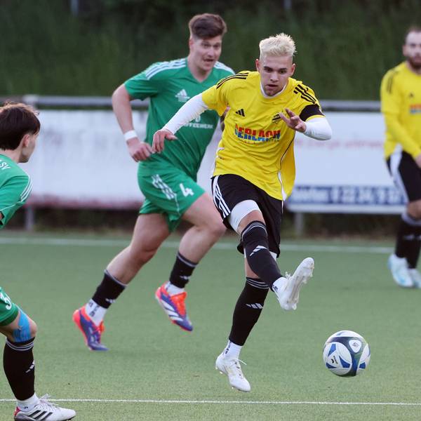 Das Foto zeigt einen Spieler des VfR Bachem im gelben Trikot, der von zwei Horremern in grünen Trikots am Abspiel nicht gehindert werden kann.