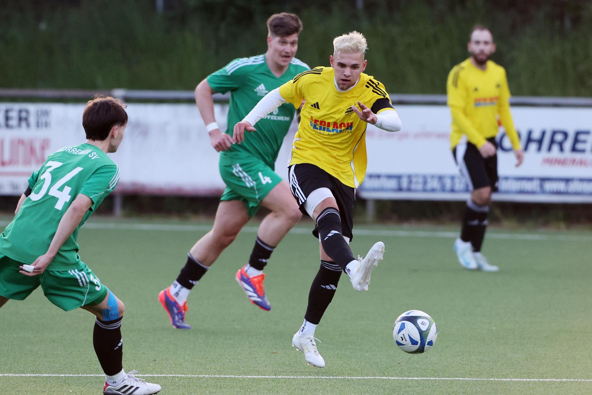 Das Foto zeigt einen Spieler des VfR Bachem im gelben Trikot, der von zwei Horremern in grünen Trikots am Abspiel nicht gehindert werden kann.