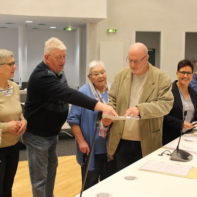 Männer und Frauen stehen vor einem Tisch und halten Papiere.