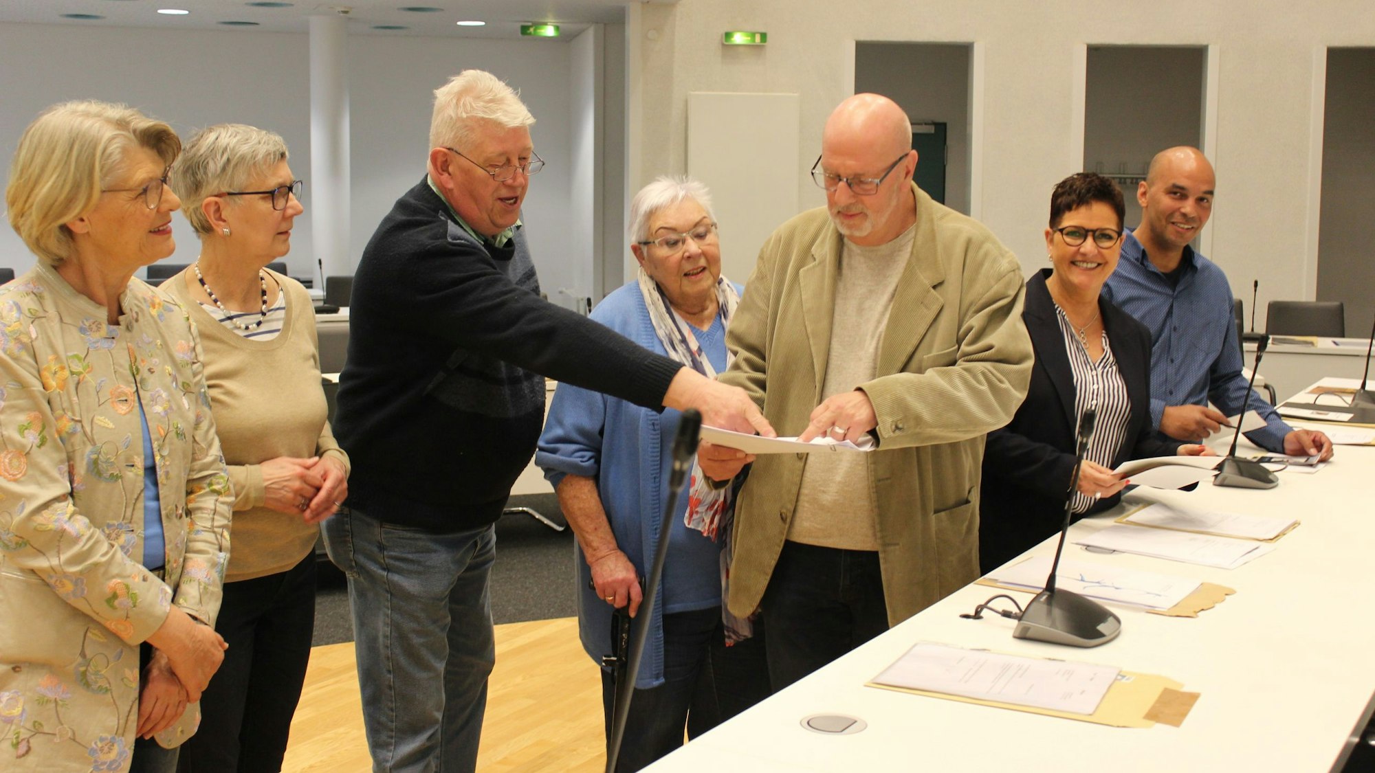 Männer und Frauen stehen vor einem Tisch und halten Papiere.