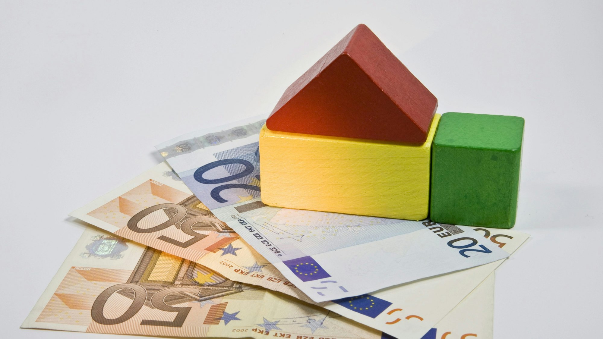 Ein Spielzeughaus aus Holz steht auf zwei 50- und einem 20-Euro-Schein. (Symbolfoto)