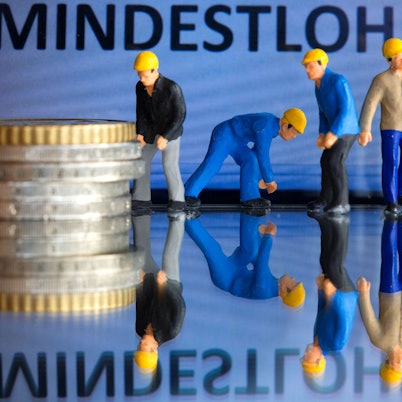 Miniaturfiguren stehen vor einem Display mit der Anzeige «Mindestlohn» (gestelltes Foto).