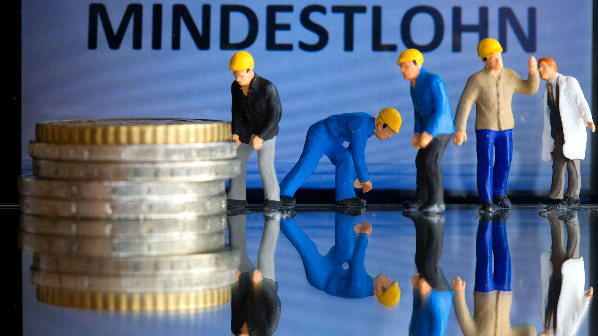 Miniaturfiguren stehen vor einem Display mit der Anzeige «Mindestlohn» (gestelltes Foto).
