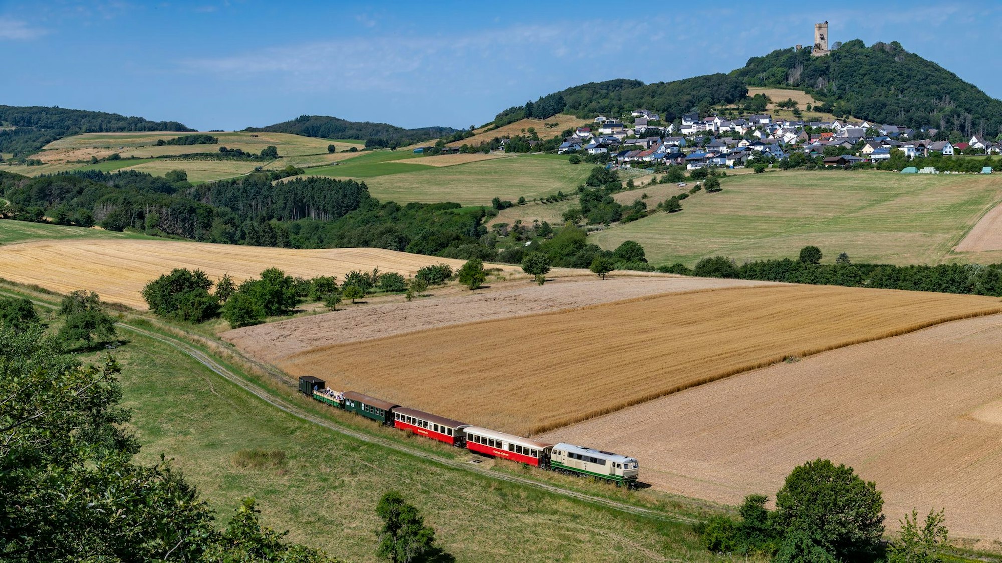 Der Vulkan-Express erschließt die Vulkanregion Laacher See - im Sommer sogar mit einem Cabriowagen. Kombinationen z.B. mit Burg Olbrück (Hintergrund) versprechen einen schönen Ausflug.