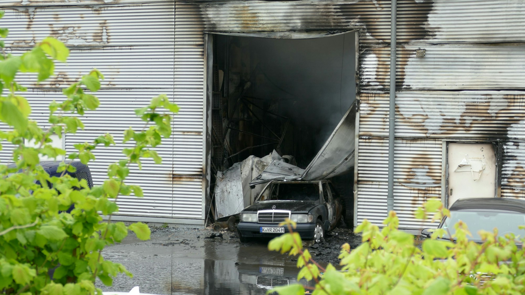 Die Halle in Niederkassel hat an ihrer Außenhülle deutliche Brandspuren. Im Tor steht ein Auto, auf das Teile des Tores gestürzt sind.