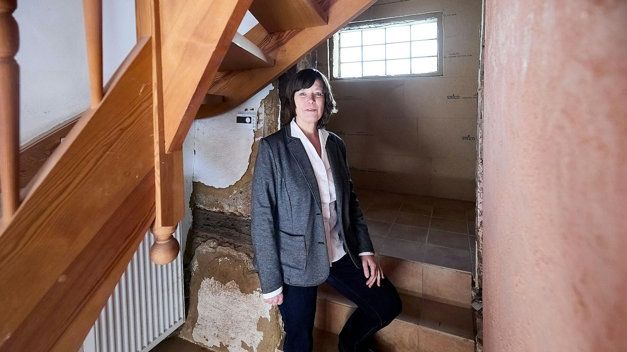 Die Frau steht in einem Haus, das Flutschäden aufweist.