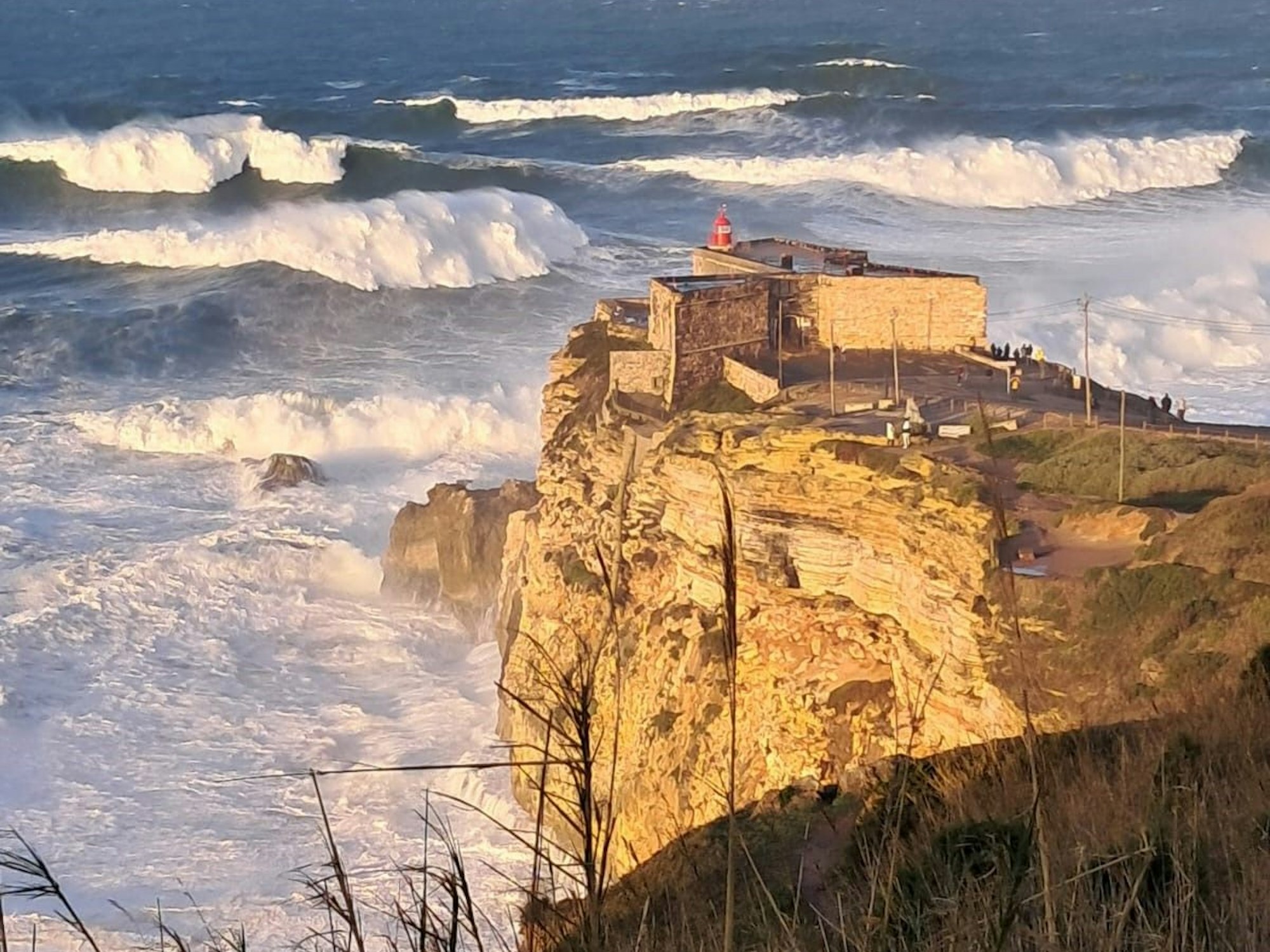 Blick auf das Küstenmassiv in Nazaré mit hohen Wellen im Hintergrund.