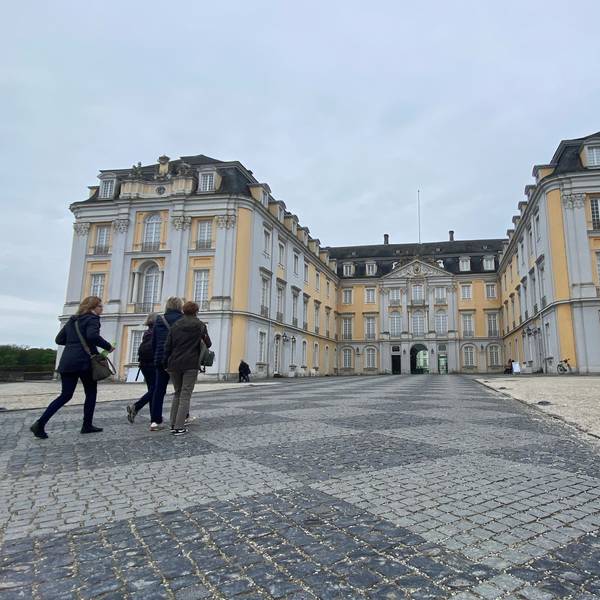 Zu sehen ist eine Gruppe von Menschen, die auf das Schloss zugehen.