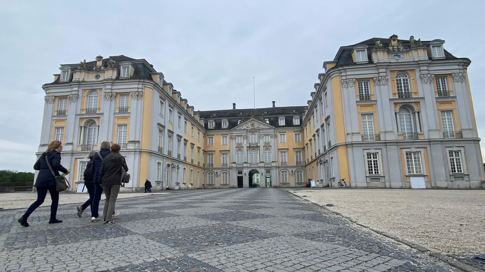 Zu sehen ist eine Gruppe von Menschen, die auf das Schloss zugehen.