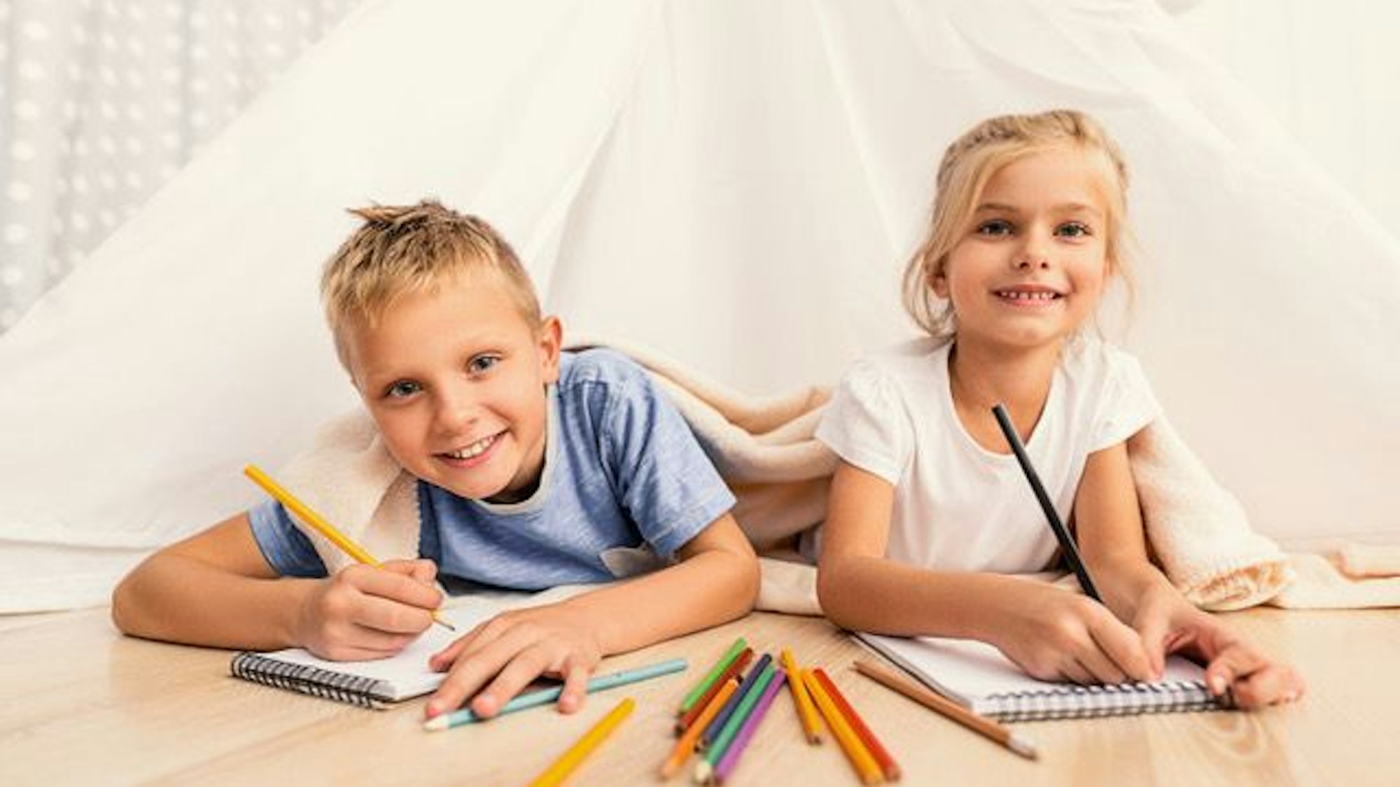 Zwei Kinder liegen auf dem Boden und haben Buntstifte in der Hand.