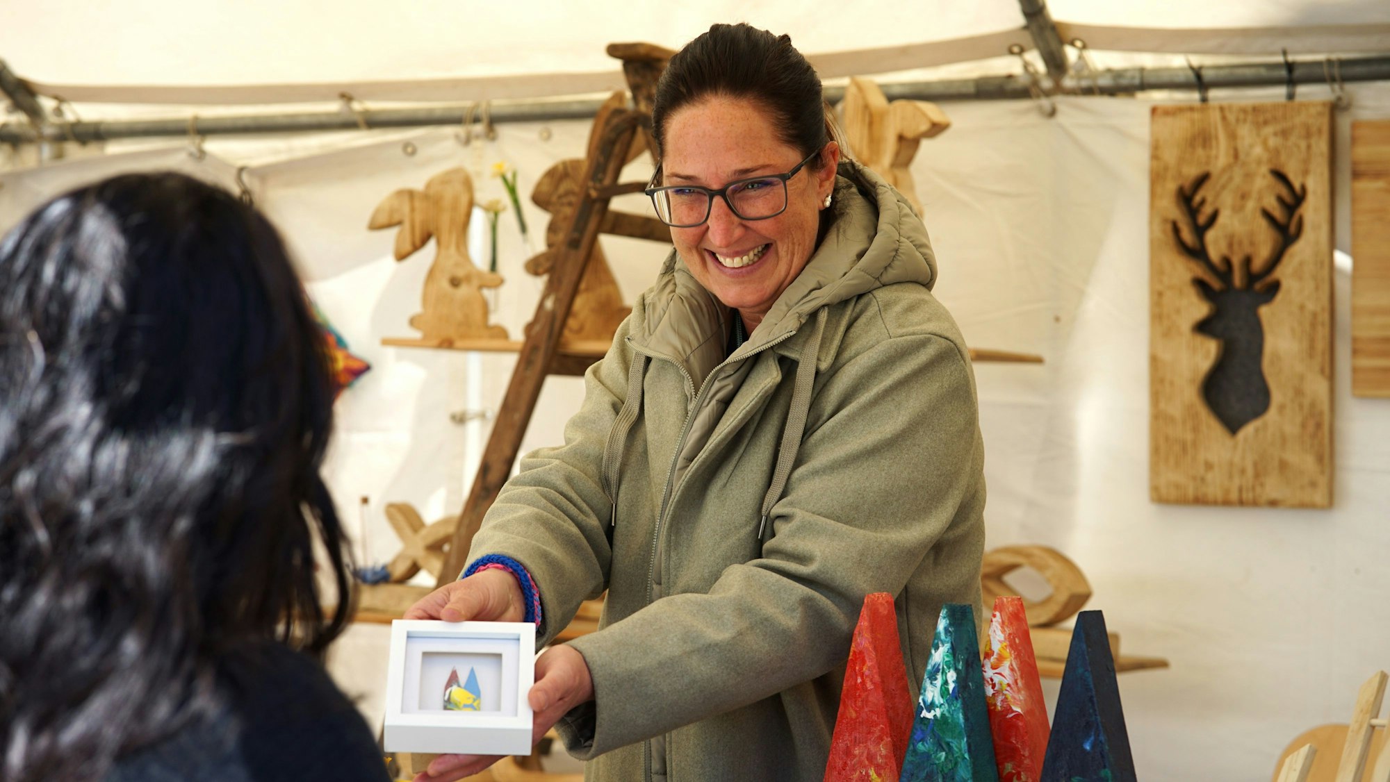 Eine Frau hinter einem Stand zeigt einer Interessentin ein Bild und lächelt.