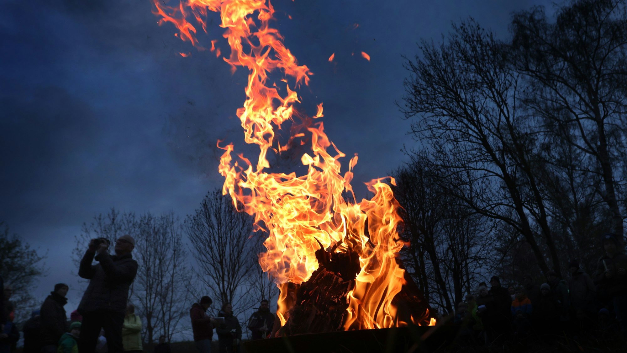 ARCHIV - 08.04.2023, Bayern, Nürnberg: Gläubige stehen während einer ökumenischen Osterfeier im Stadtteil Boxdorf um ein loderndes Osterfeuer. (zu dpa: «Osterfeuer trotz Trockenheit - Mahnung zu Vorsicht») Foto: Karl-Josef Hildenbrand/dpa +++ dpa-Bildfunk +++