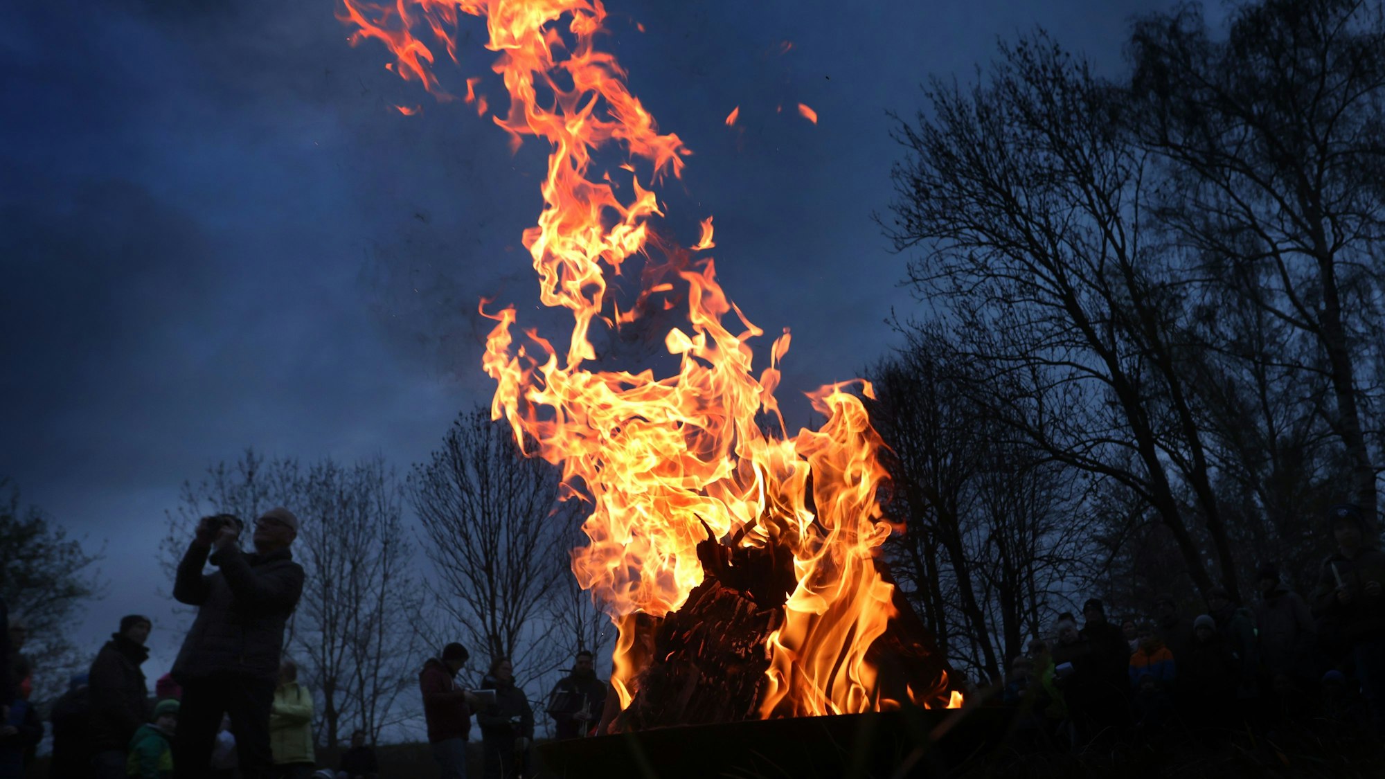Gläubige stehen um ein loderndes Osterfeuer.