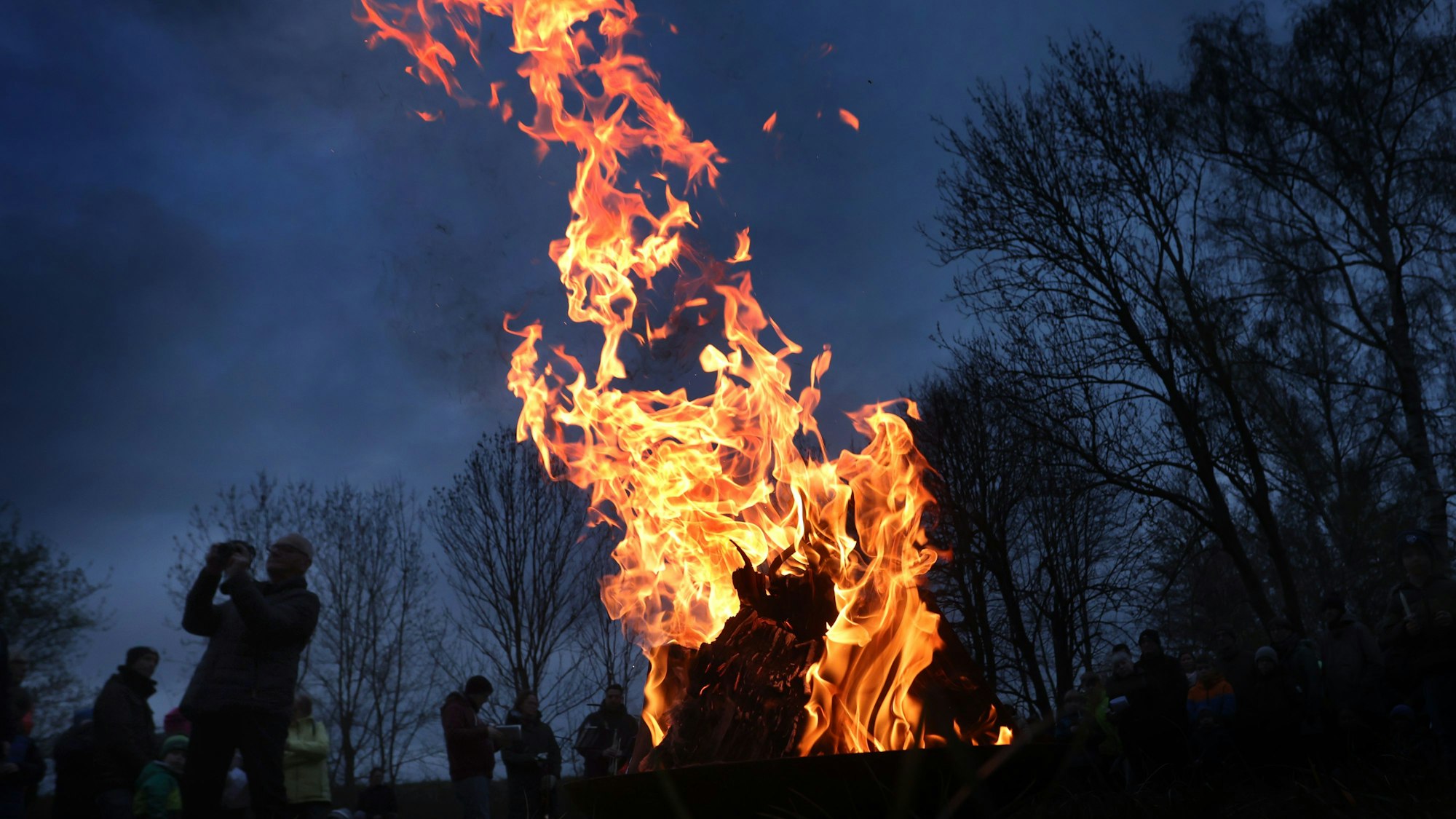 Gläubige stehen um ein loderndes Osterfeuer.