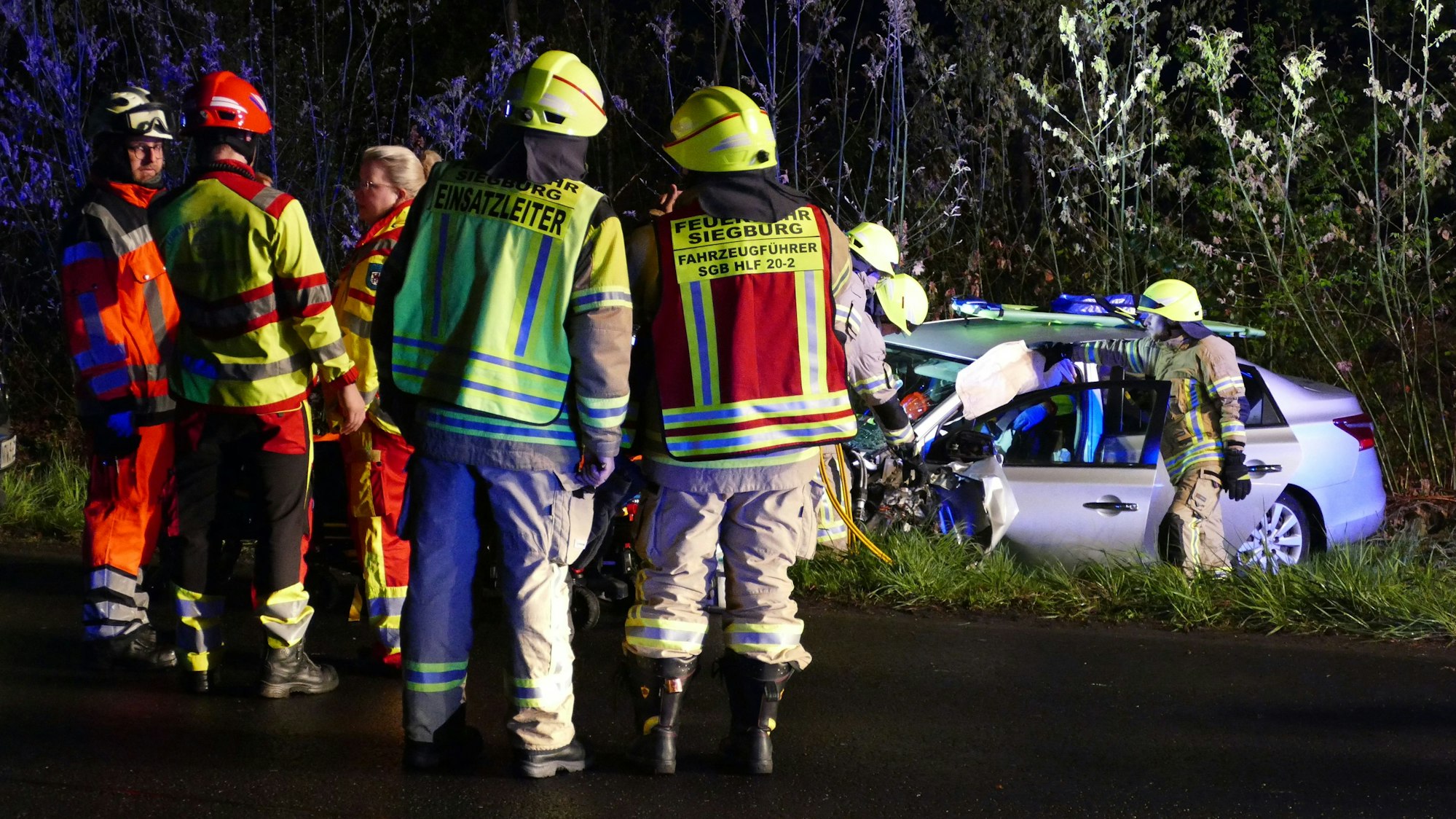 Feuerwehrleute stehen neben einem verunglückten Auto.