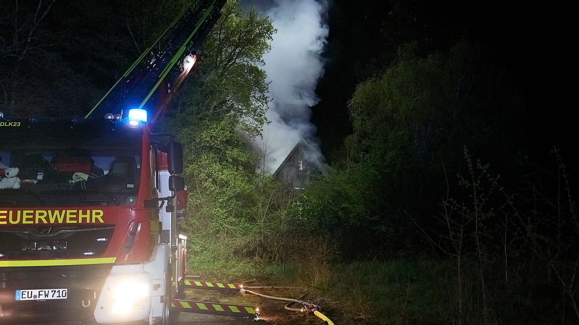 Die Drehleiter ist in Stellung gegangen. Im Hintergrund steigt eine Rauchwolke aus dem brennenden Gebäude.