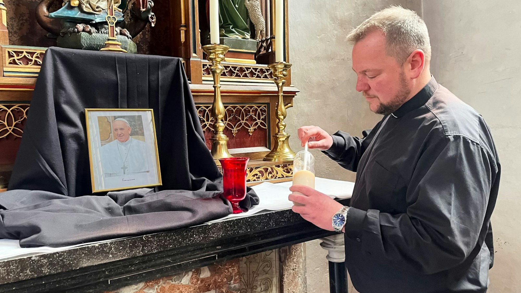 Vor einem Bild des Papstes, das auf einem schwarzen Tuch aufgestellt wurde, entzündet der Pfarrer eine Kerze.