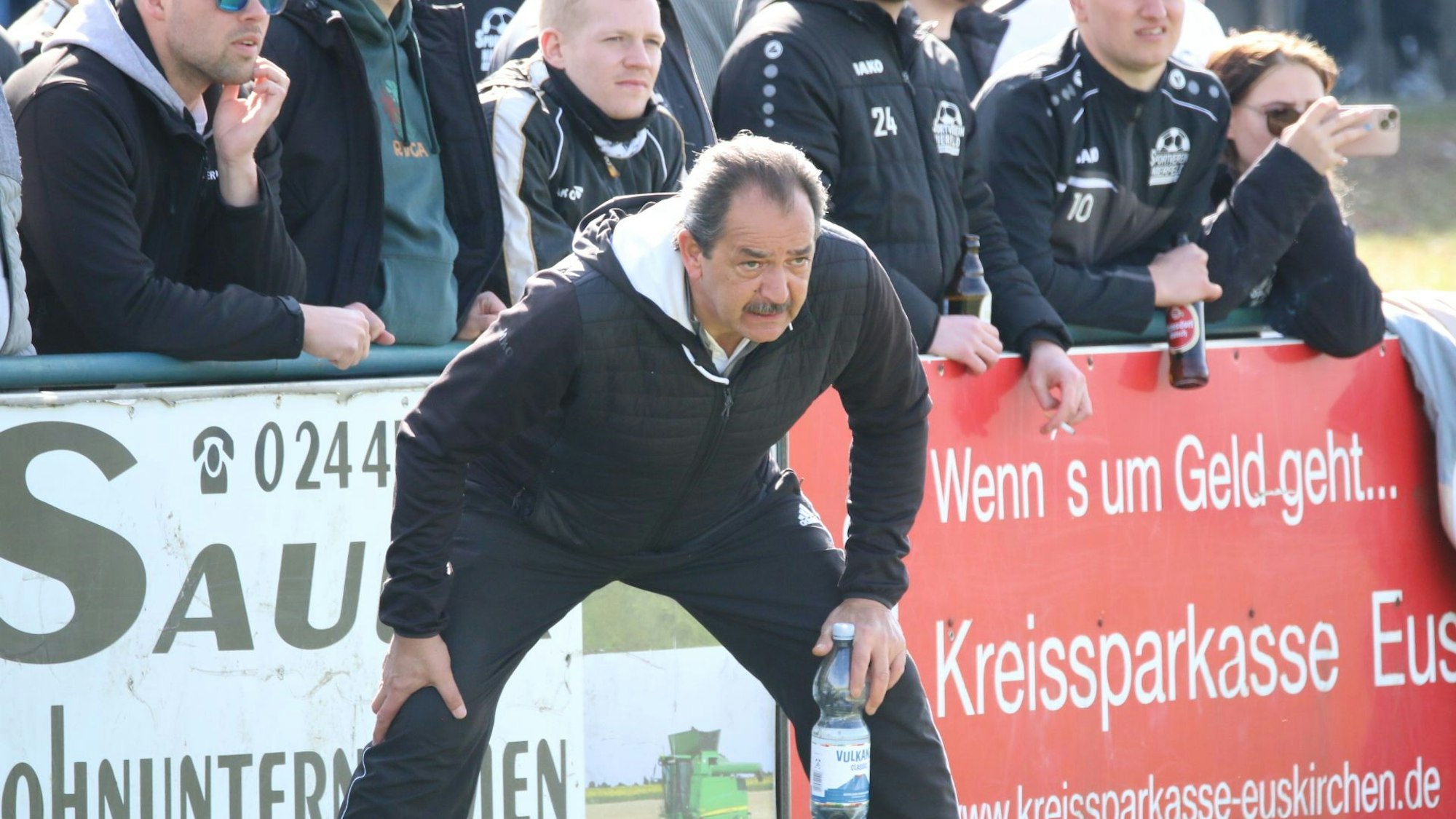 Steht nach vorne gebeugt und breitbeinig da, beide Hände auf die Knie gestützt, mit einer Hand hält er noch eine Flasche: Nierfelds Trainer Dirk Scheer.