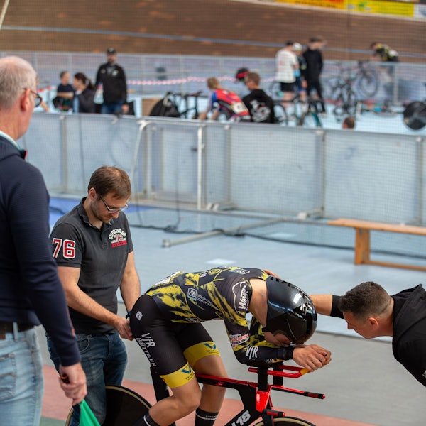 Mika Lohmar kauert vornübergebeugt und konzentriert auf seinem Rennrad, während sein Trainer mit ihm redet.