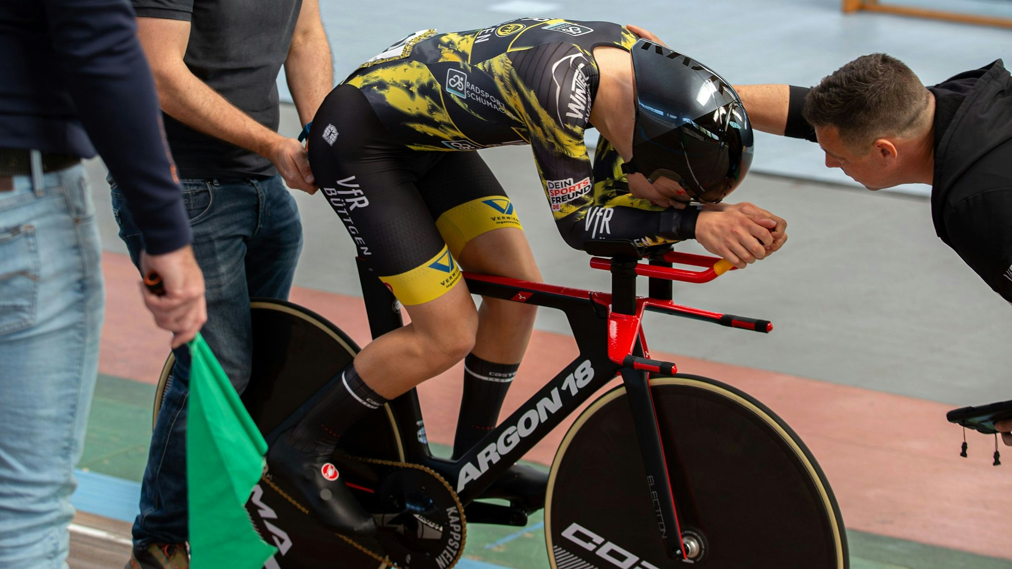 Mika Lohmar kauert vornübergebeugt und konzentriert auf seinem Rennrad, während sein Trainer mit ihm redet.