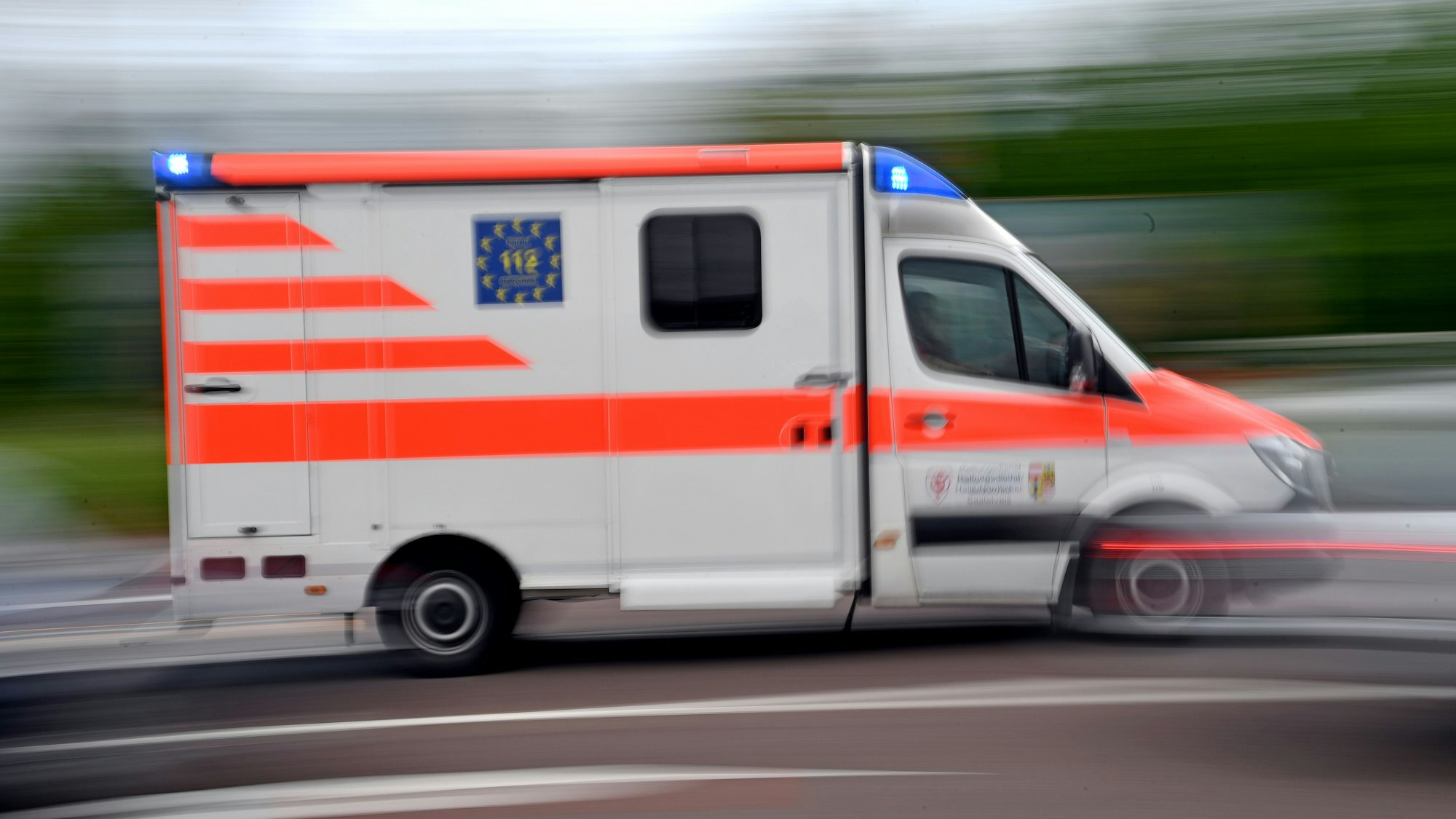 Ein Krankenwagen fährt mit Blaulicht über eine Straße.