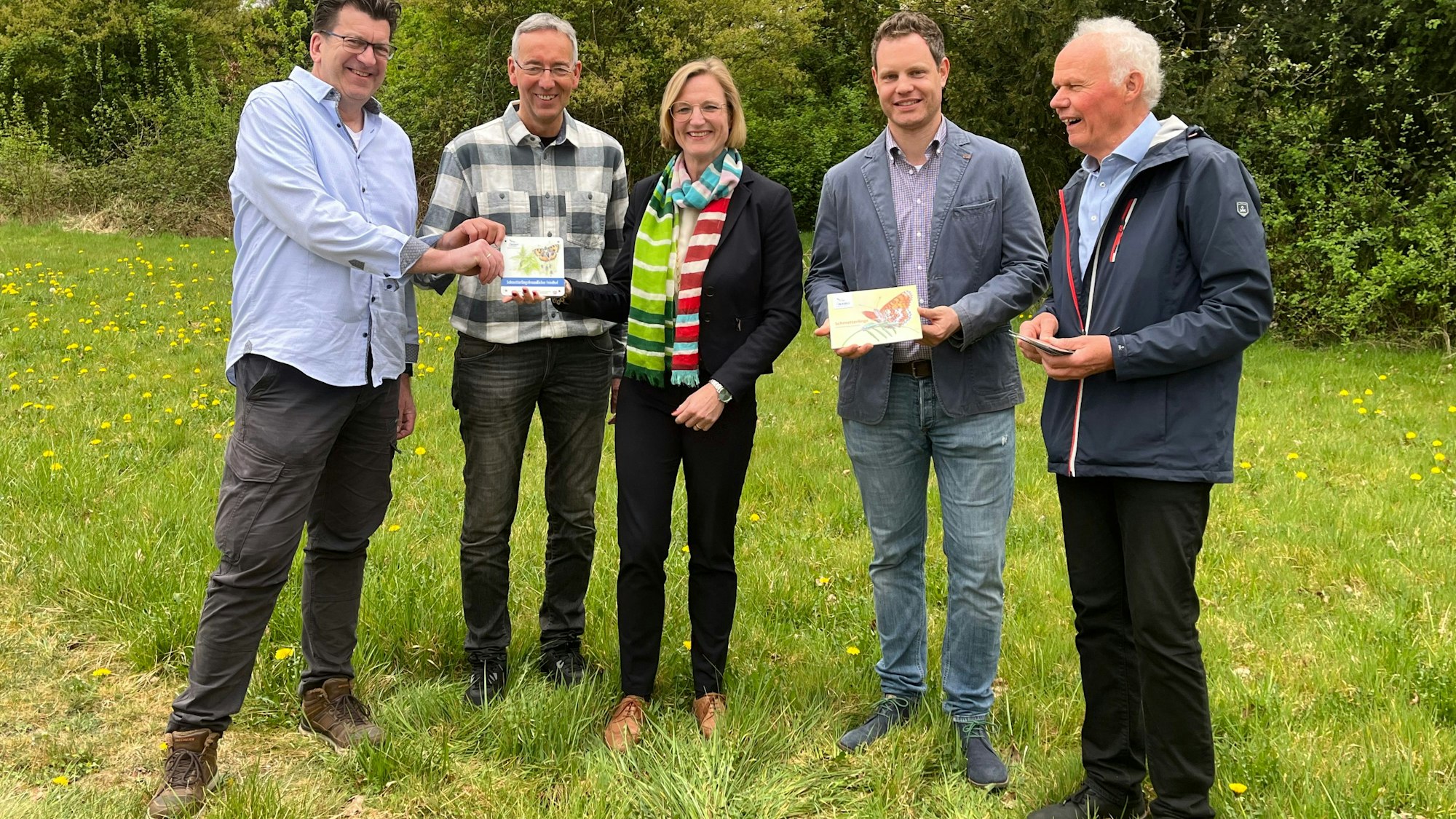 Vier Männer und eine Frau stehen auf einer Grünfläche.