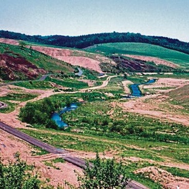 Durch ein leergeräumtes Tal ohne Bäume und Häuser fließt ein Bach.