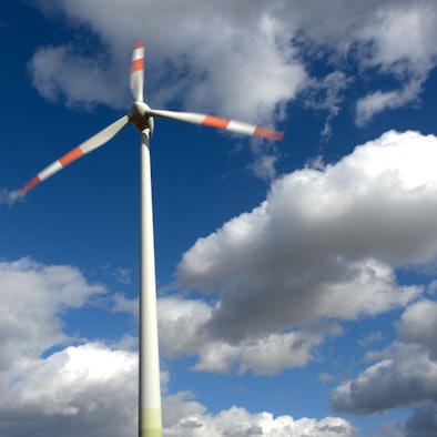 Ein Windrad dreht sich vor weiß-blauem Himmel.