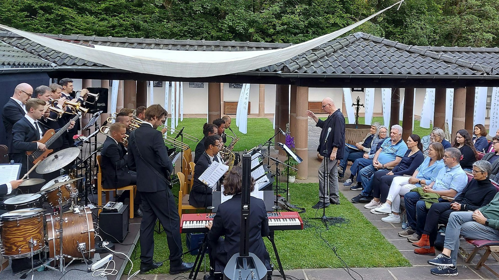 Das Orchester spielt im Freien vor einer sitzenden Menschenmenge.