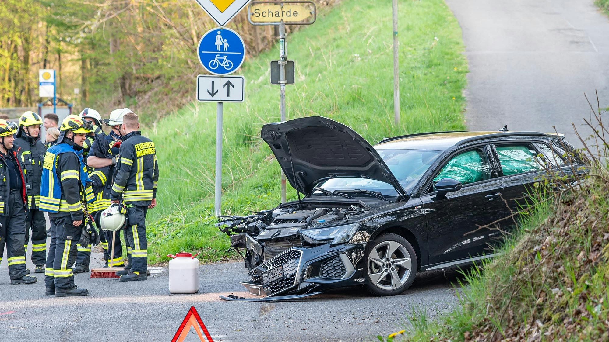 Mehrere Einsatzleute der Feuerwehr betrachten ein zerstörtes Fahrzeug nach einem Verkehrsunfall.
