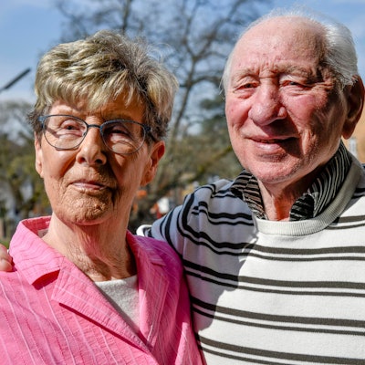 Ein älteres Ehepaar steht in der Sonne und lächelt.