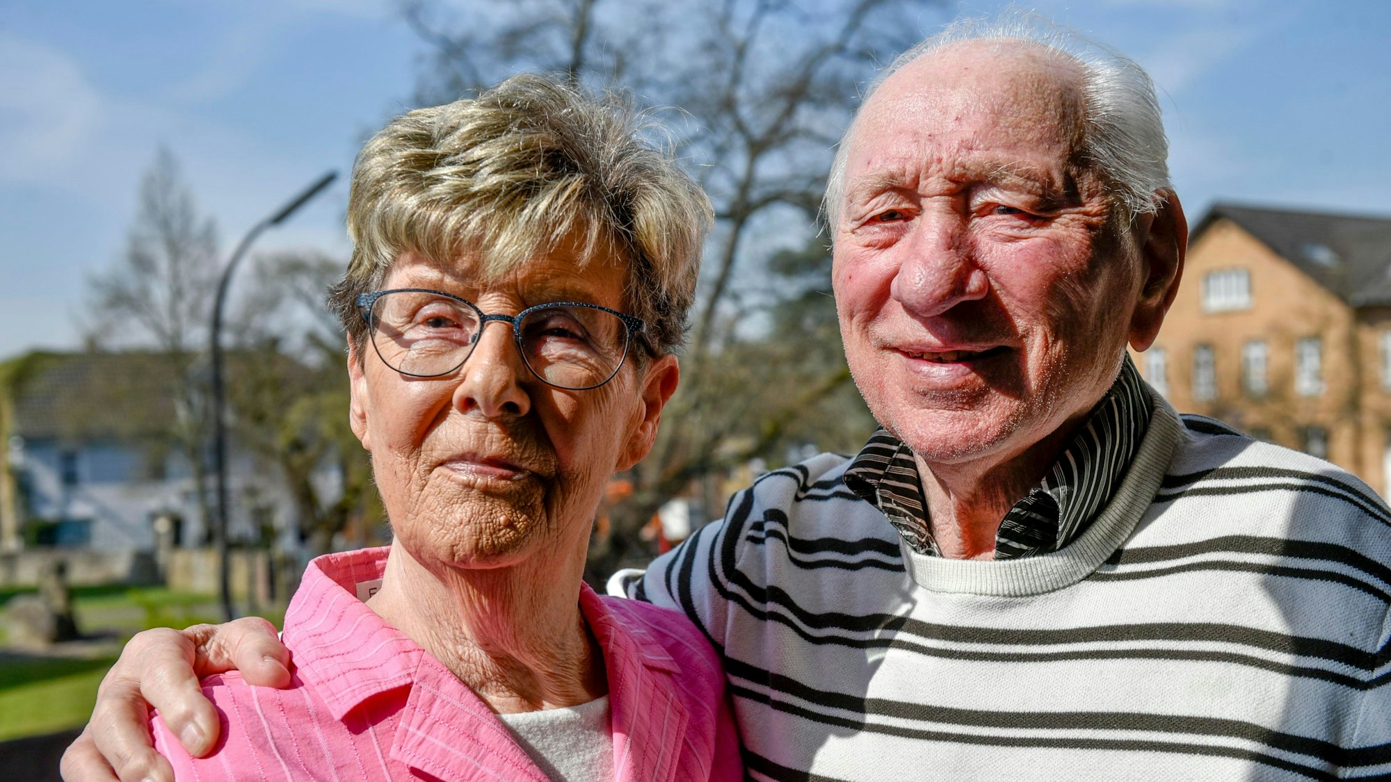 Ein älteres Ehepaar steht in der Sonne und lächelt.