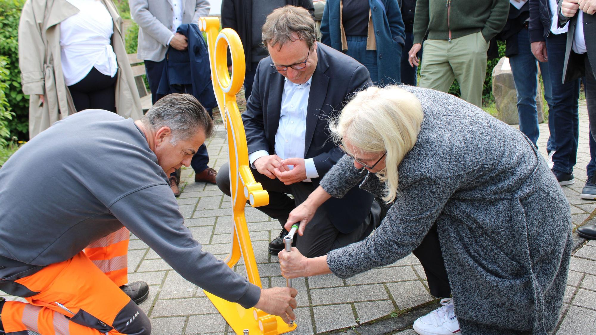 Verkehrsminister Oliver Krischer und Bürgermeisterin Claudia Wieja bringen einen Aufsteller für mehr Sicherheit am Knoten Bachstraße/ Rathausstraße/ Am Bungert an.