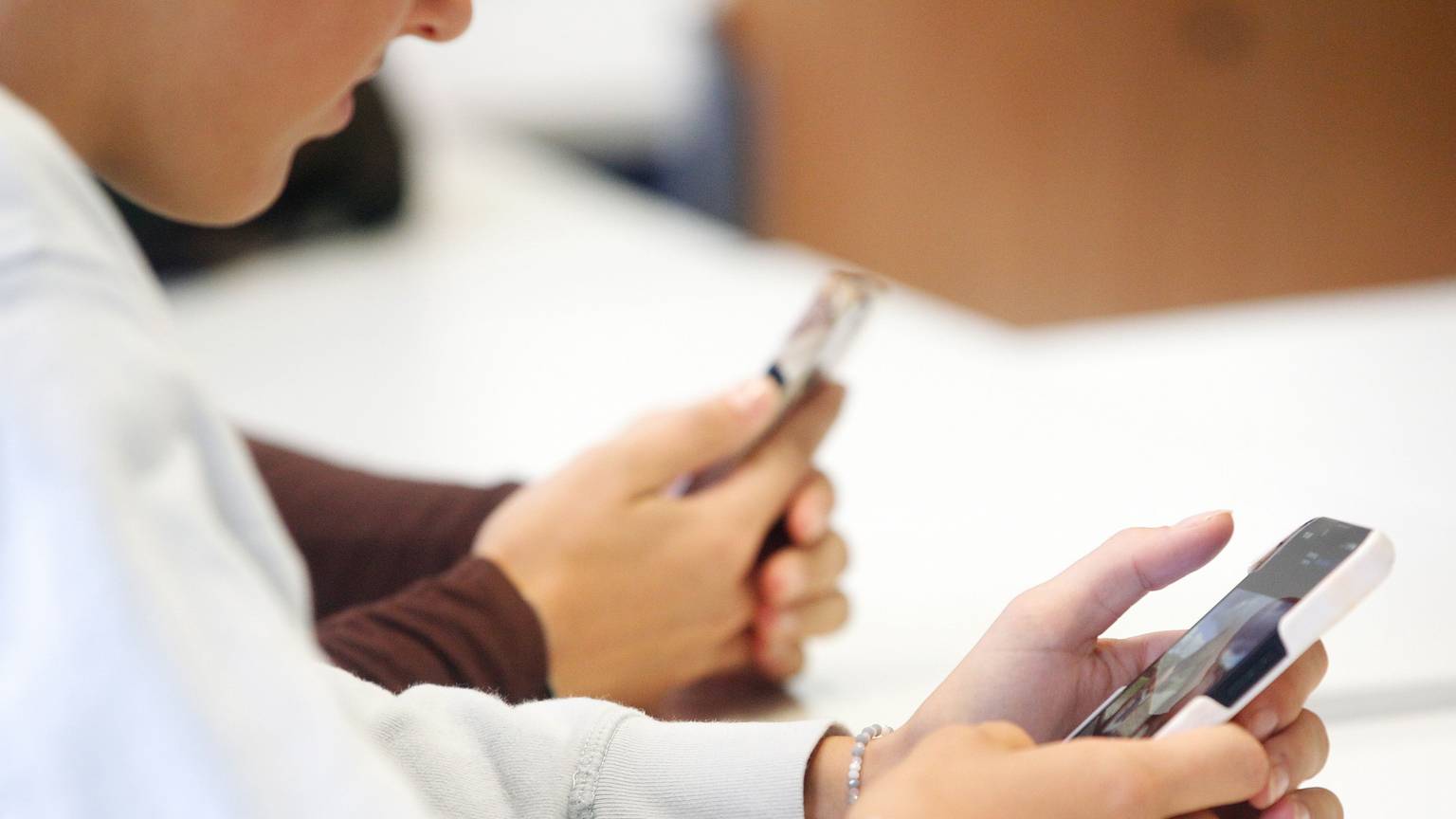 Schülerinnen benutzen während eines Vortrags ihr Smartphone im Unterricht.