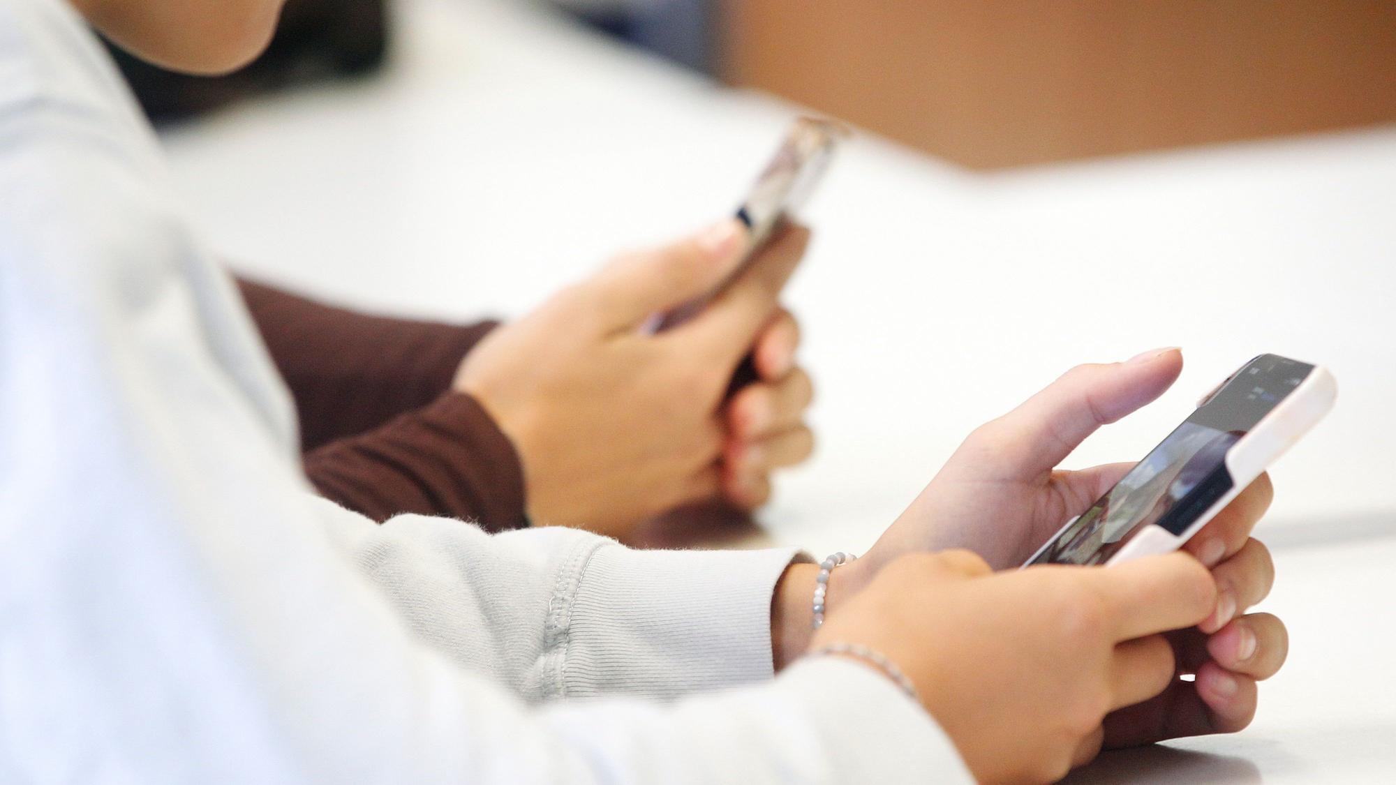 Schülerinnen benutzen während eines Vortrags ihr Smartphone im Unterricht.